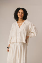 Woman wearing a white blouse and skirt set against a plain background