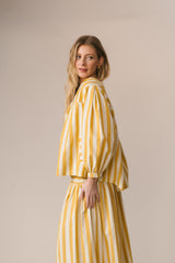 Woman wearing a yellow and white striped outfit against a beige background