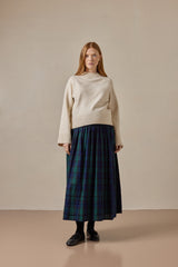 Woman wearing a cream sweater and green and blue tartan skirt against a beige background